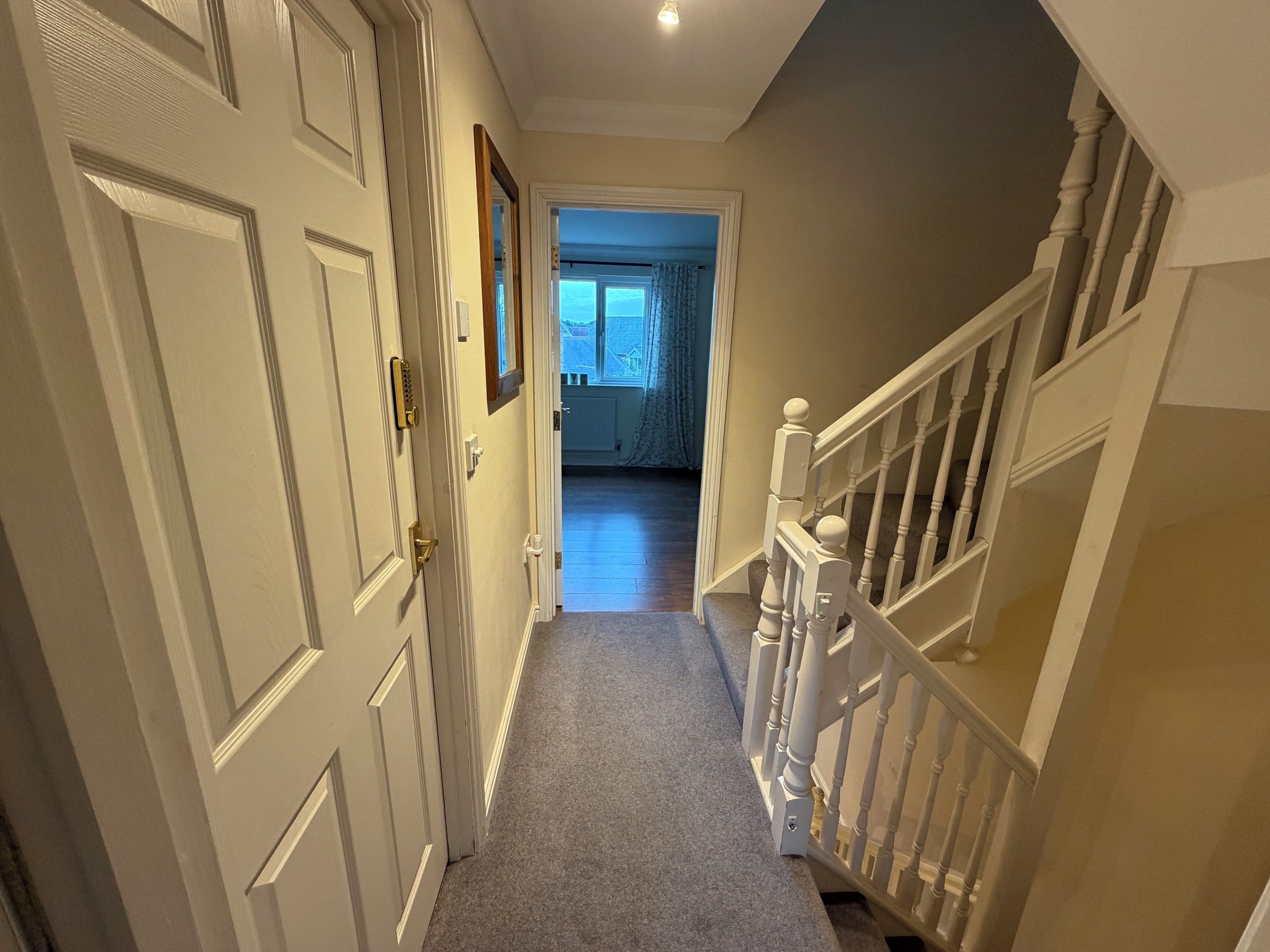 A hallway with a carpeted floor, white doors, and a staircase with white railings.