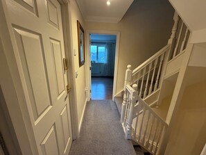 A hallway with a carpeted floor, white doors, and a staircase with white railings.