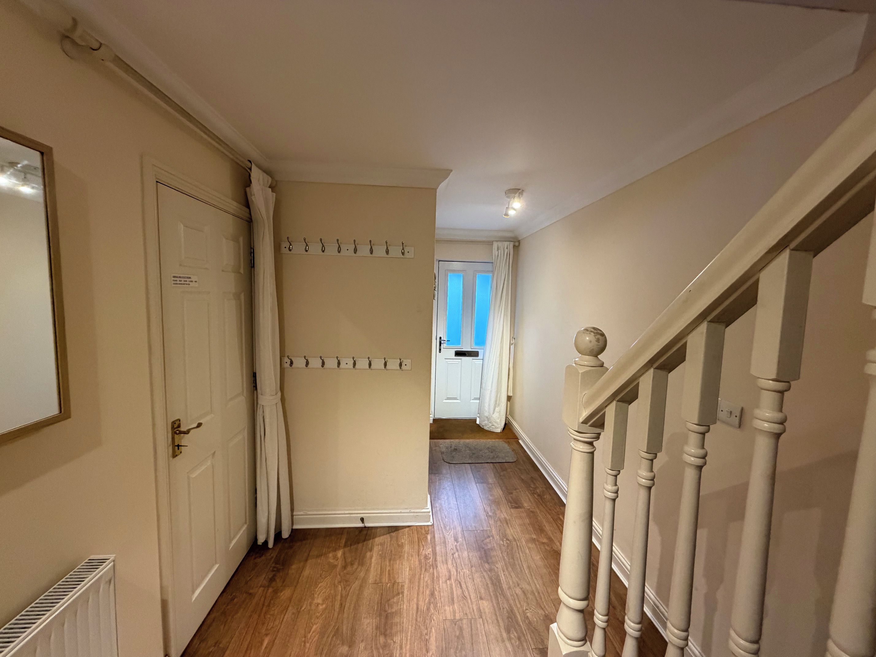 A hallway with a wooden floor, a white door, a coat rack, and a staircase with white balusters.