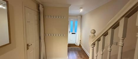 A hallway with a wooden floor, a white door, a coat rack, and a staircase with white balusters.