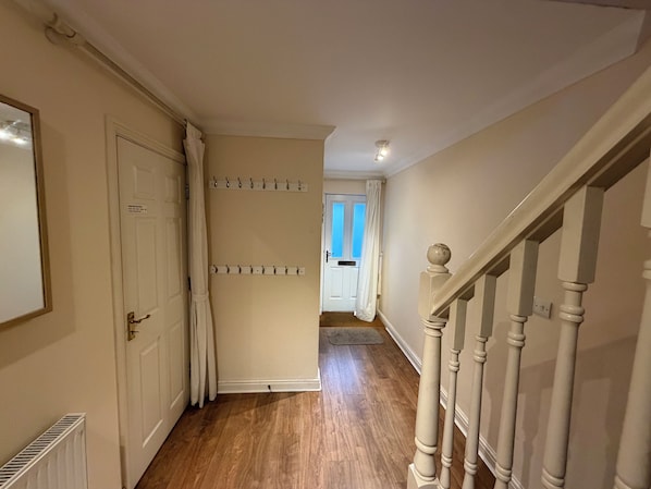 A hallway with a wooden floor, a white door, a coat rack, and a staircase with white balusters.