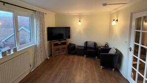 A living room with a television, seating, a radiator, and a window with curtains.