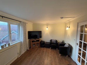 A living room with a television, seating, a radiator, and a window with curtains.
