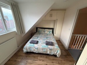 A small, single-bed room with a sloped ceiling, a window with curtains, a radiator, and a wooden floor. - Mountfield - For families, walkers and cyclists (Freshwater)