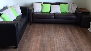 A living room with a dark brown leather sofa, two matching armchairs, and a wooden floor. - Mountfield - For families, walkers and cyclists (Freshwater)