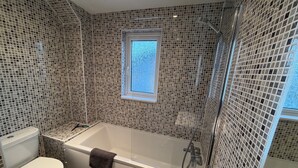 A bathroom with a bathtub, toilet, and a window.