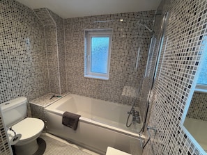 A bathroom with a bathtub, toilet, and a window.