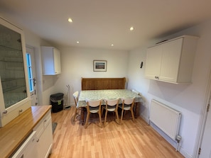 A compact kitchen with a dining table, chairs, and a radiator.