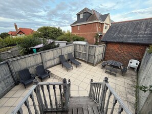 A backyard with a wooden deck, outdoor seating, and a brick house in the background. - Mountfield - For families, walkers and cyclists (Freshwater)
