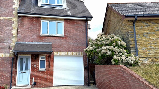 A two-story house with a garage, a brick facade, and a small garden with white flowers.