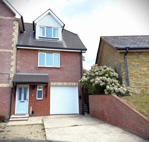 A two-story house with a garage, a brick facade, and a small garden with white flowers. - Mountfield - For families, walkers and cyclists (Freshwater)
