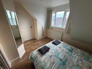 Un dormitorio con cama, ventana, radiador y puerta que da a una escalera.