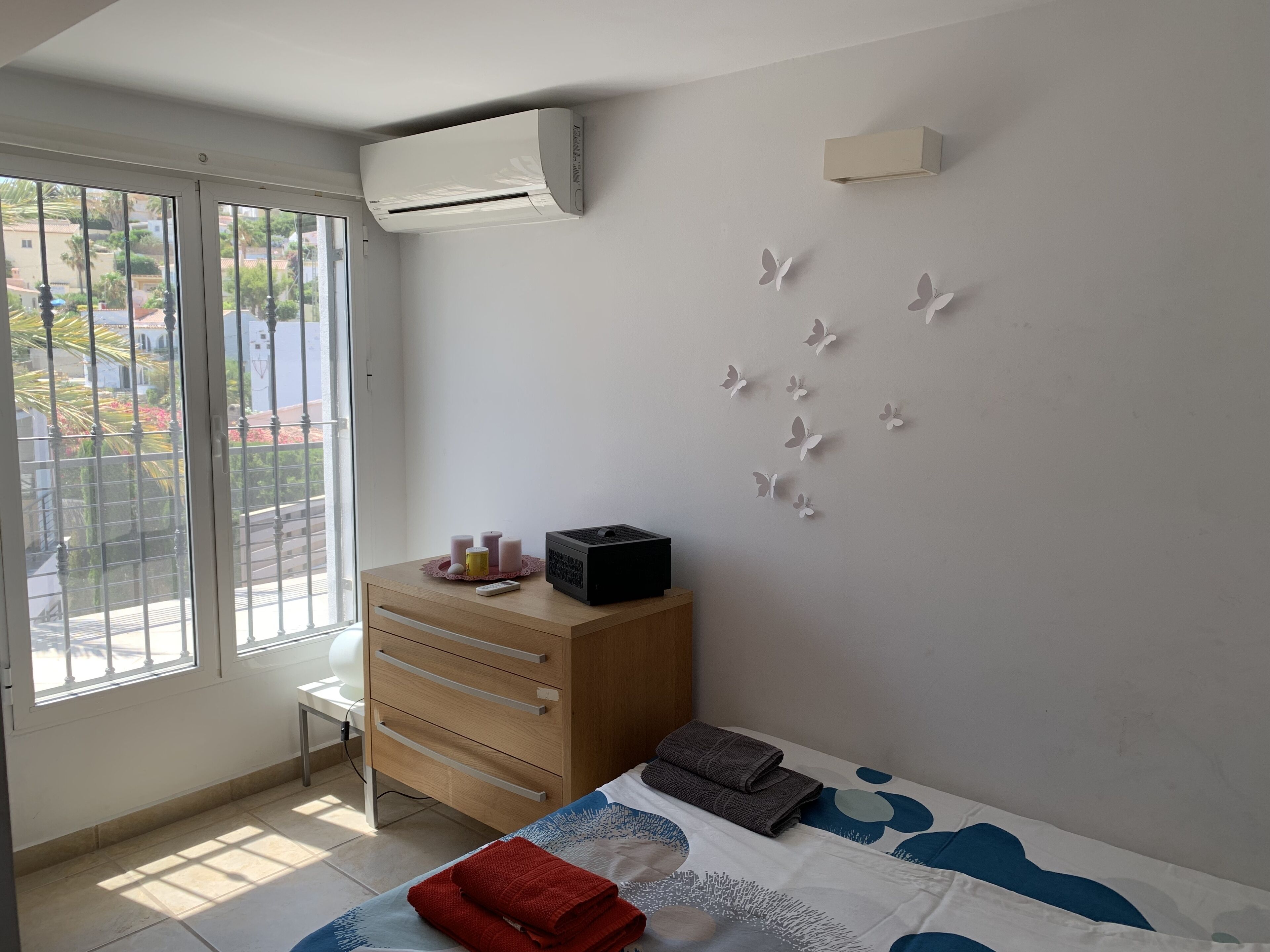 A bedroom with a bed, a dresser, an air conditioner, and a window with a view of the outside.