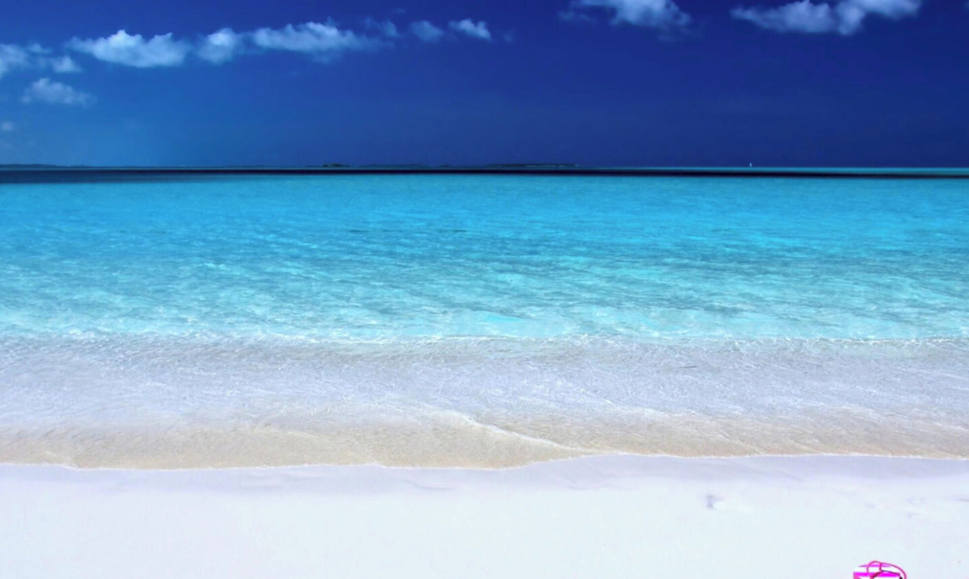 A beach with the word "HOLIDAY" written in the sand and a pair of pink flip-flops nearby.