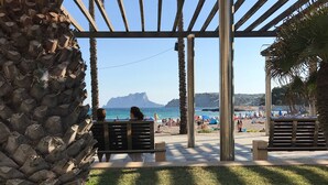 A beachside seating area with a wooden pergola, palm trees, and a view of the sea and mountains in the background. - Magnificent villa with private pool for 6 people in Moraira - Bénissa (Moraira)