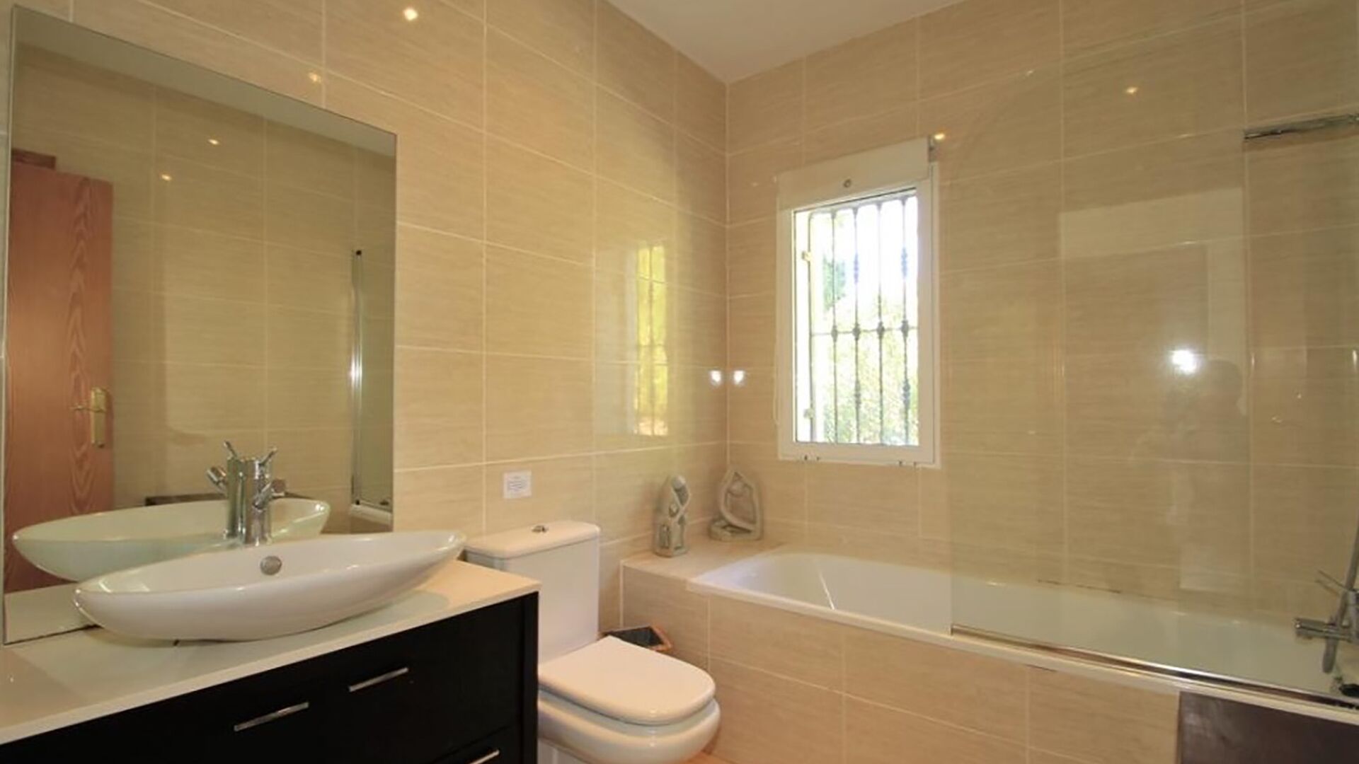A modern bathroom with a large mirror, two sinks, a toilet, and a bathtub.