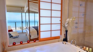 A bathroom with a large bathtub, a shower, and a view of a balcony with a bed and a chair. - Adelaide Luxury Beach House (Henley Beach)