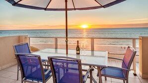A table with chairs and an umbrella on a balcony overlooking the ocean at sunset. - Adelaide Luxury Beach House (Henley Beach)