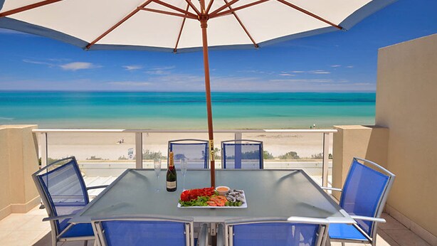 A table with chairs and an umbrella overlooking a beach. - Adelaide Luxury Beach House (Henley Beach)