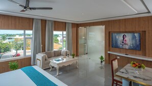 A modern hotel room with a bed, a sofa, a coffee table, a TV, and a balcony with a city view. - Hotel SS Palace (Rameshwaram)