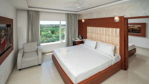 A hotel room with a large bed, a chair, a desk with a phone, and a window with curtains. - Hotel SS Palace (Rameshwaram)