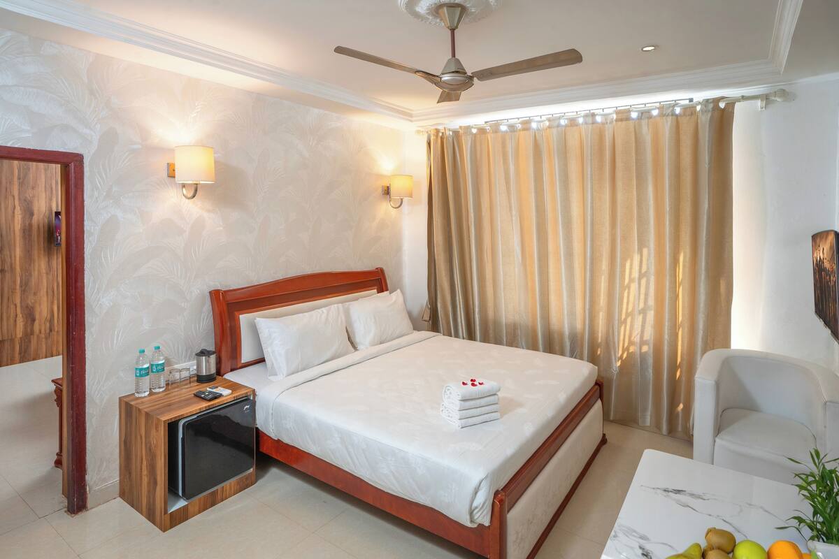A hotel room with a bed, bedside table, nightstand, TV, and a seating area with a table and chairs.