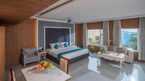 A modern hotel room with a large bed, a sofa, a coffee table, and a view of the city. - Hotel SS Palace (Rameshwaram)