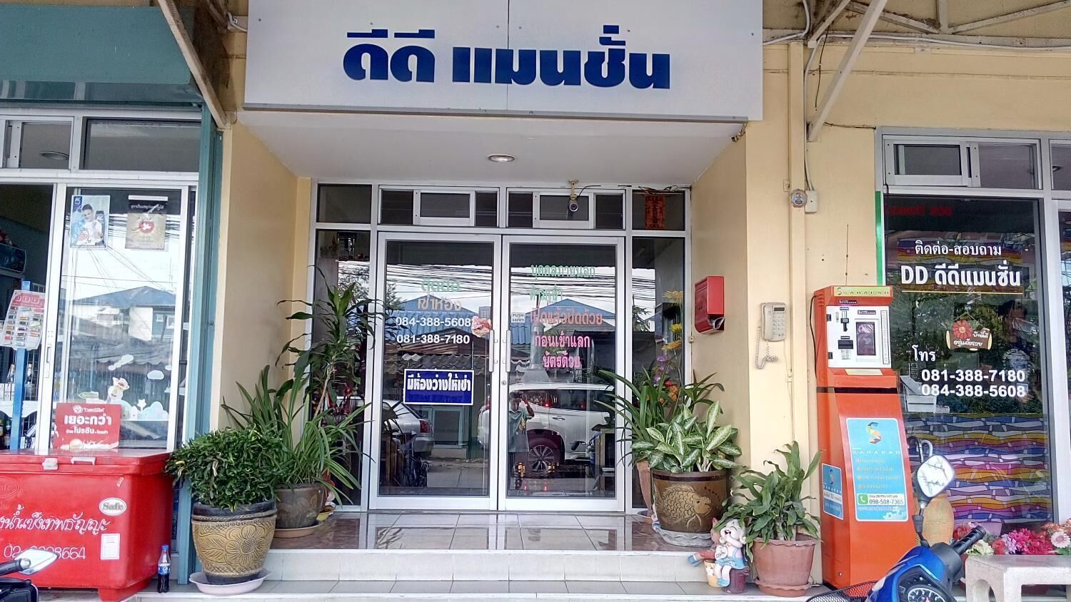 A storefront with a sign in a foreign language, a glass door entrance, and several potted plants outside.