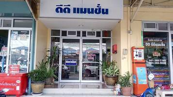 A storefront with a sign in a foreign language, a glass door entrance, and several potted plants outside.