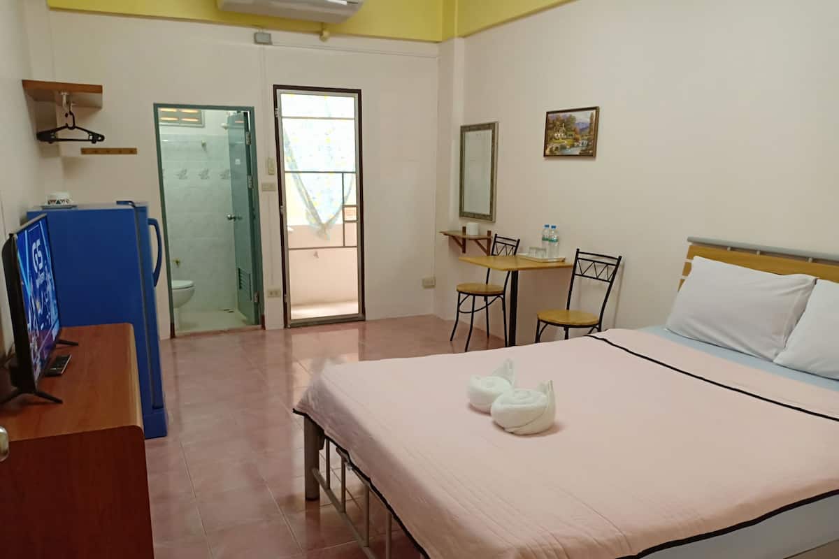 Une chambre d’hôtel comprenant un lit, un bureau avec un ordinateur, une chaise, une petite table avec une chaise, une salle de bain avec une porte en verre et une fenêtre.