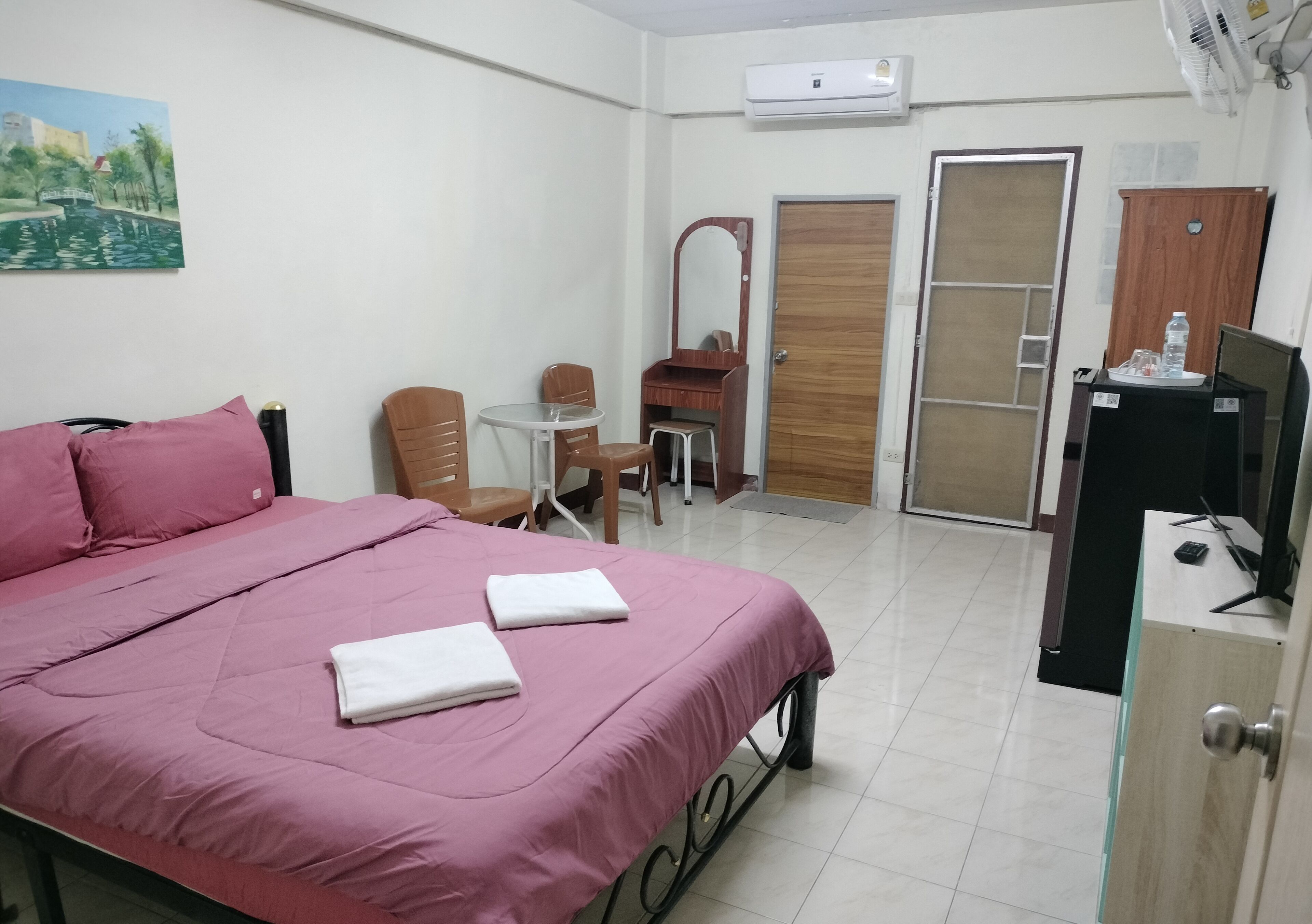 Une chambre d’hôtel comprenant un lit, une petite table, une chaise, un miroir, une armoire et un appareil de climatisation.