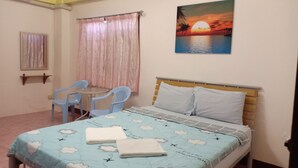 Een slaapkamer met een bed, een bureau met stoelen, een schilderij van een zonsondergang en een raam met gordijnen.
