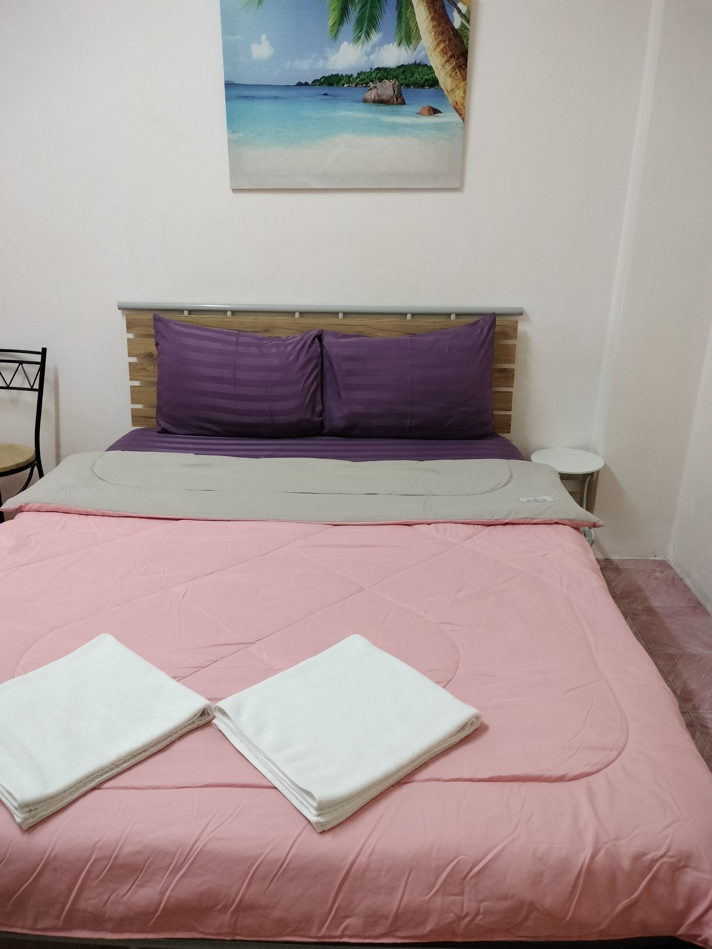 A neatly made bed with pink bedding and two white towels, a wooden headboard, and a small bedside table with a lamp.