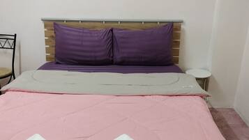 A neatly made bed with pink bedding and two white towels, a wooden headboard, and a small bedside table with a lamp.