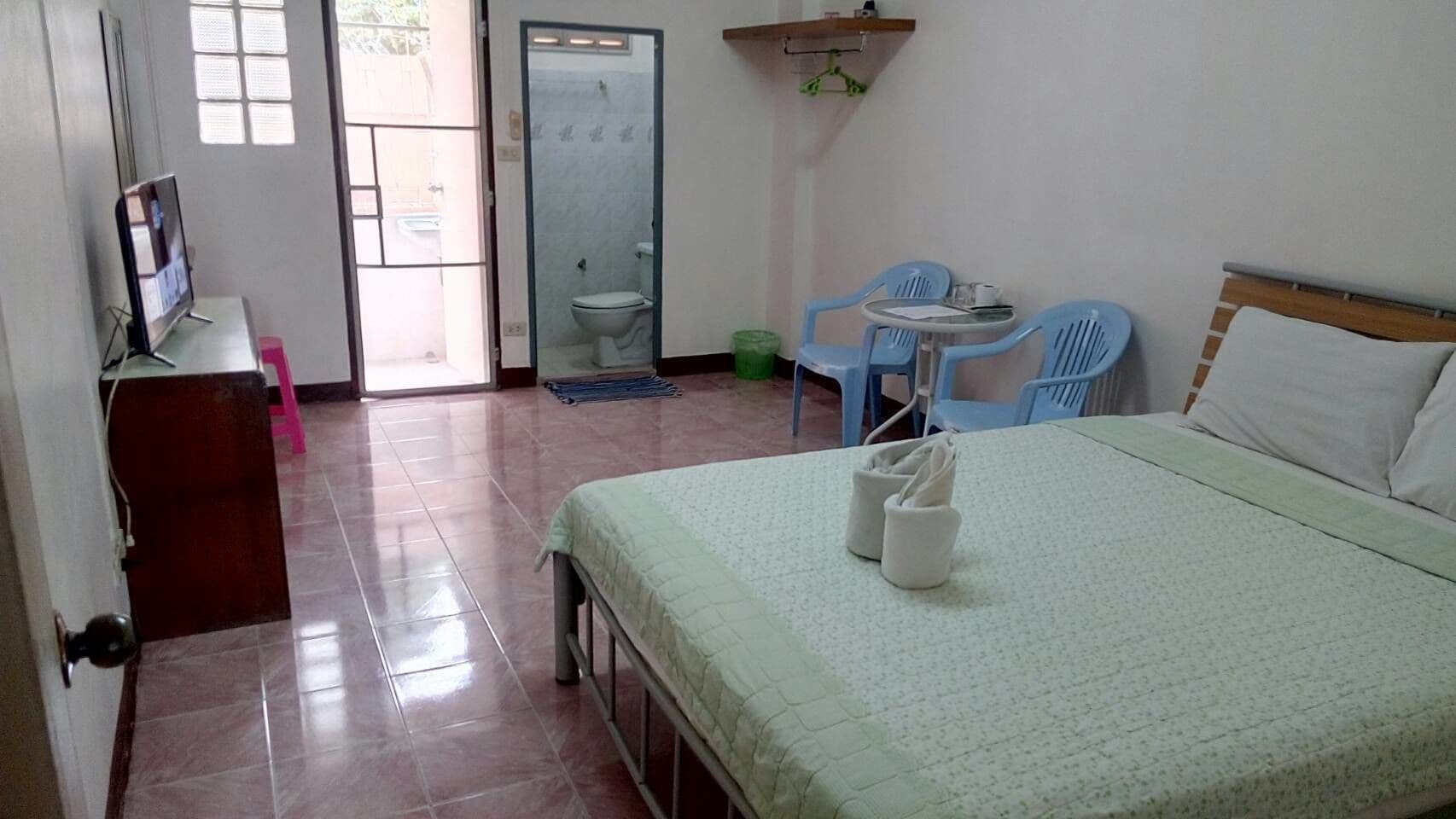 A hotel room with a bed, a desk with a TV, a bathroom with a toilet and sink, and two chairs.