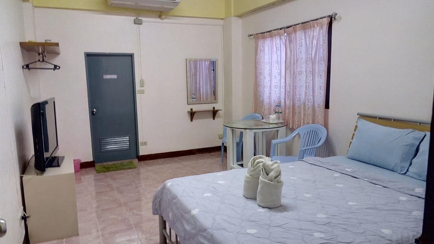 Une chambre d’hôtel avec un lit, une petite table, une chaise, un téléviseur et une porte.