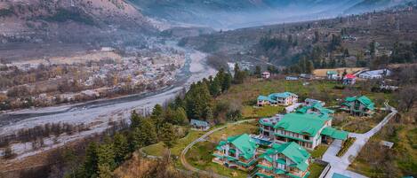 A mountainous area with a river, a small town, and several green-roofed buildings.