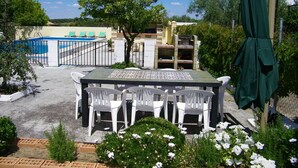 Área de piscina com mesa e cadeiras, cercada por vegetação e um muro.