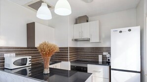 A modern kitchen with white cabinets, a black countertop, a white refrigerator, and a microwave. - Fidalsa Relax Pool your Refuge (Torrevieja)