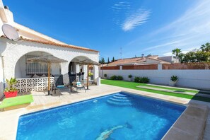 A swimming pool with a patio area, a white building with arches, and a green lawn.