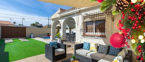 An outdoor patio with wicker furniture, a pool, and a covered area with arches.