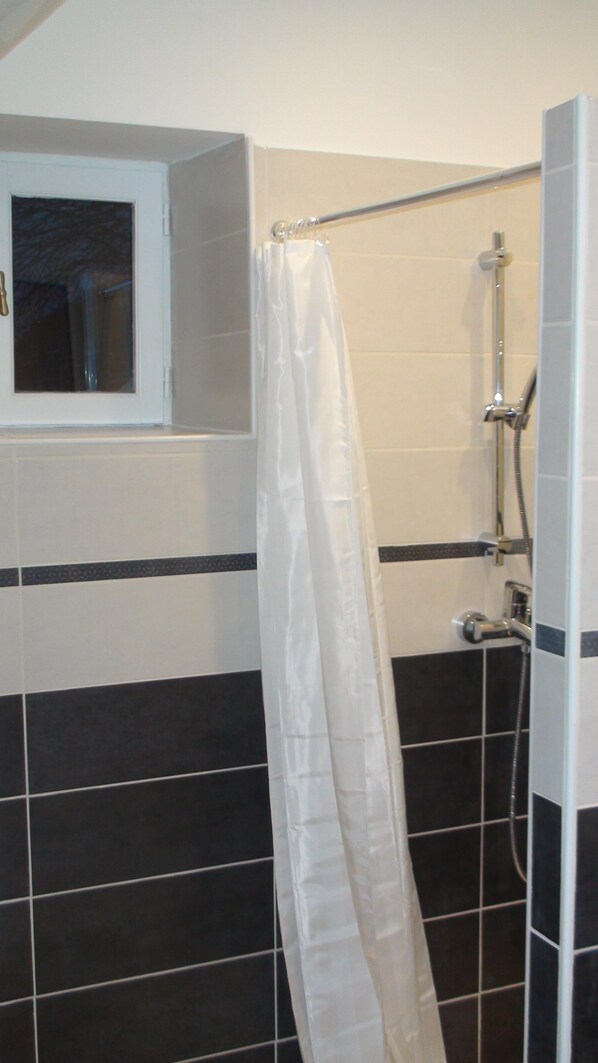 Een badkamer met douche, raam en betegelde wanden.