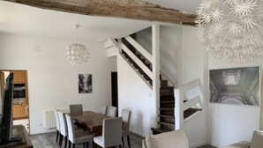 A modern living room with a wooden dining table, beige sofas, a staircase, and a chandelier. - Cottage in an old farmhouse (Frémainville)