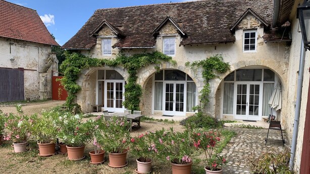 A stone building with arched windows and a tiled roof. There are potted plants in the courtyard. - Cottage in an old farmhouse (Frémainville)
