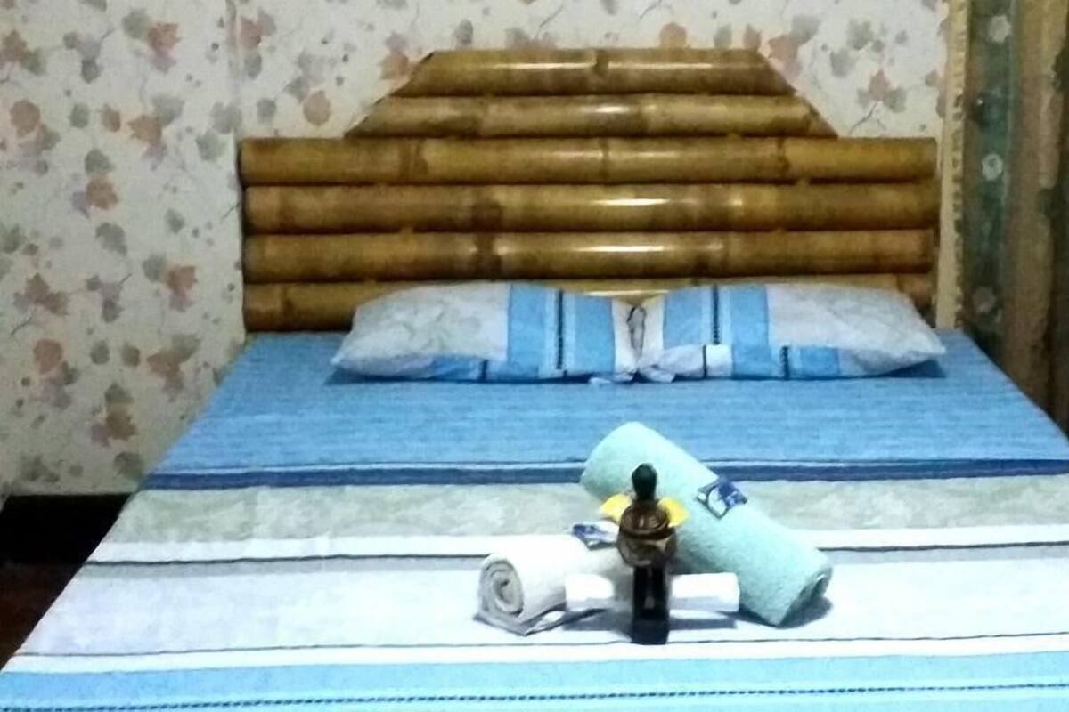 Un lit avec une tête de lit en bois, une literie bleue et une serviette enroulée.