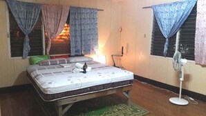 Una habitación con una cama individual, un ventilador de pie y una ventana con cortinas.