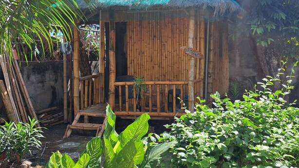 Una cabaña de bambú con techo de paja, un banco de madera y un letrero que dice 