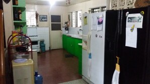 Cocina compacta con refrigerador, estufa y pileta. Cuenta con alacenas verdes y un ventanal con persianas.