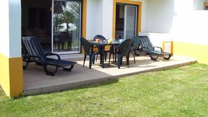 Patio esterno con tavolo e sedie, una porta scorrevole in vetro e un piccolo giardino.