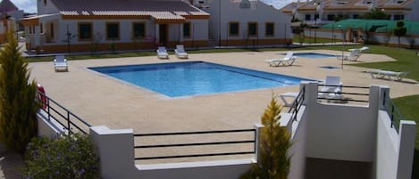 A swimming pool with lounge chairs, a white building with yellow trim, and a clear sky.